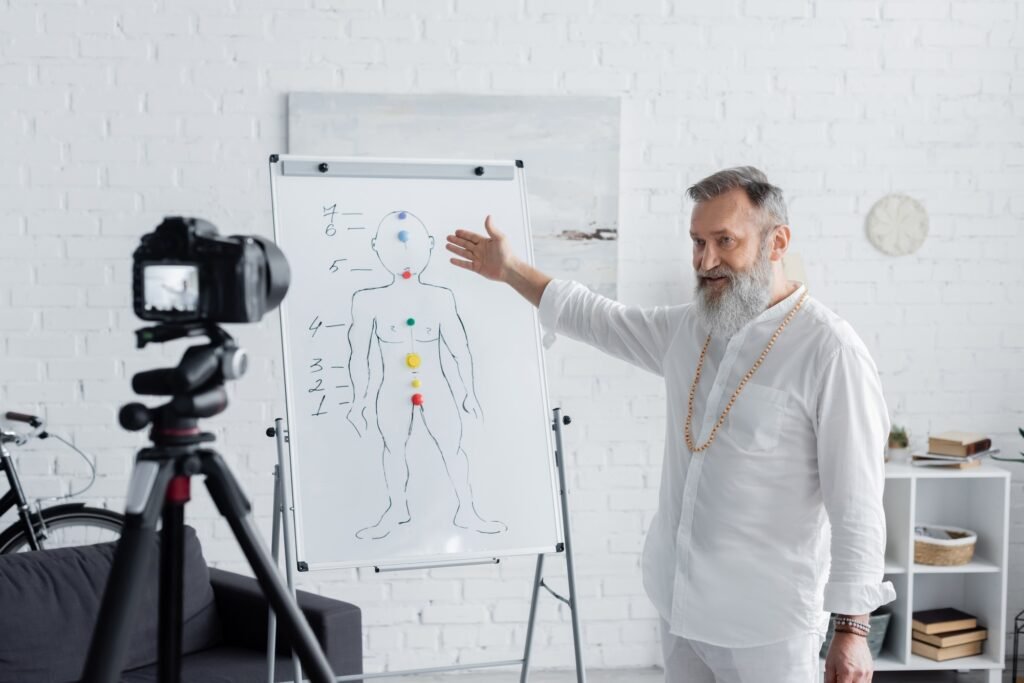 senior ayurveda coach pointing at human chakras system on flip chart in front of digital camera